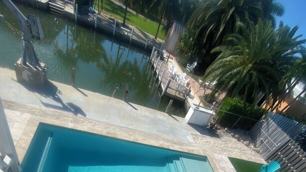 Una piscina con un pequeño jacuzzi contiguo, rodeada por una terraza de piedra y palmeras.