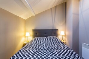 Relax in a stylish room with a large bed and geometric patterned bedspread, featuring a tufted headboard and bedside lamps.