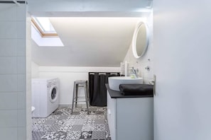 Features a skylight above the washing machine, a sink with mirror, toilet, and stool.