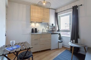 Compact kitchen with a modern design, featuring a stainless steel range hood, coffee maker, and dishwasher, and a dining area with a table and chairs.