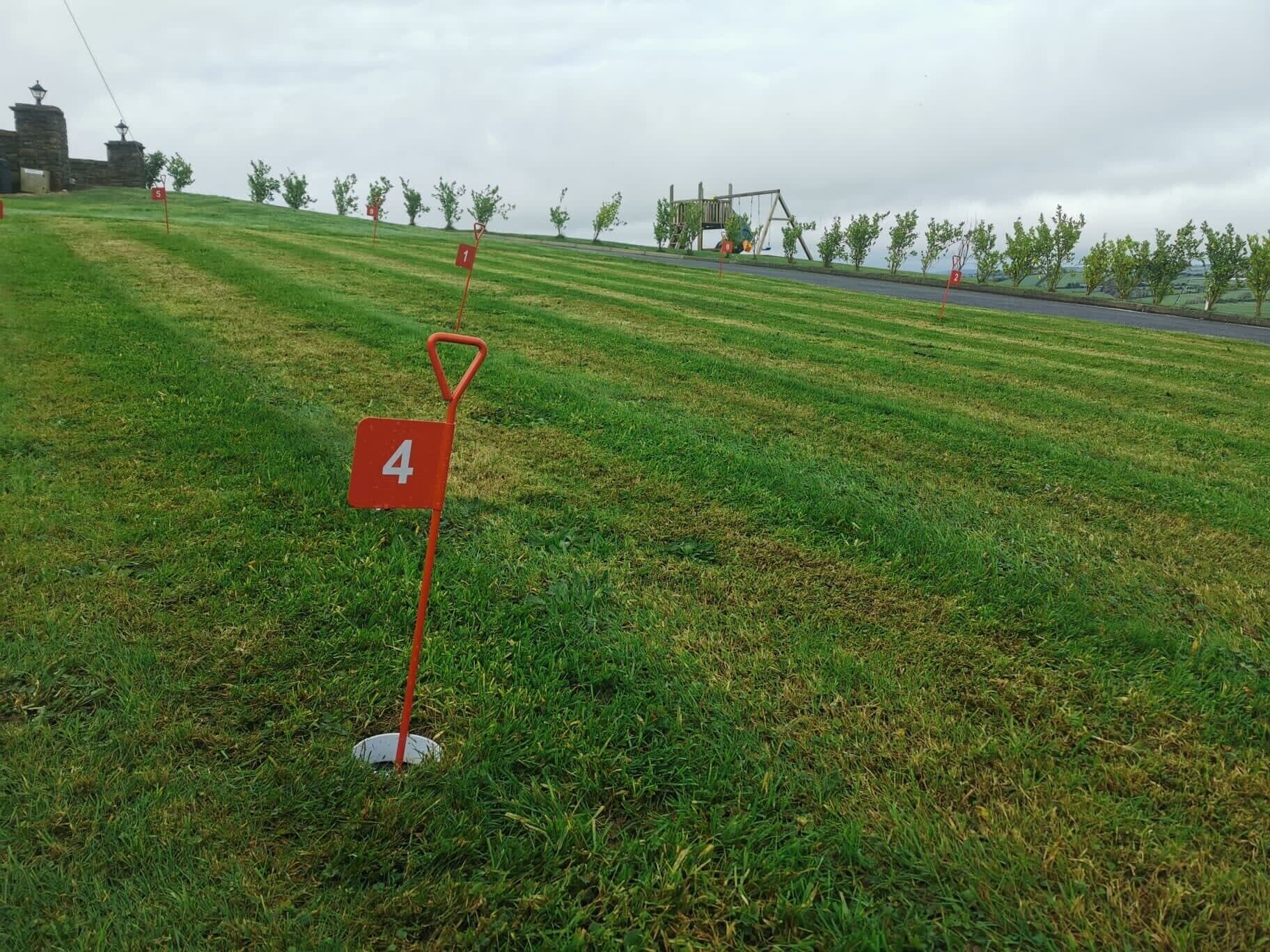 A grassy area with numbered markers, a playground, and a stone building in the background.