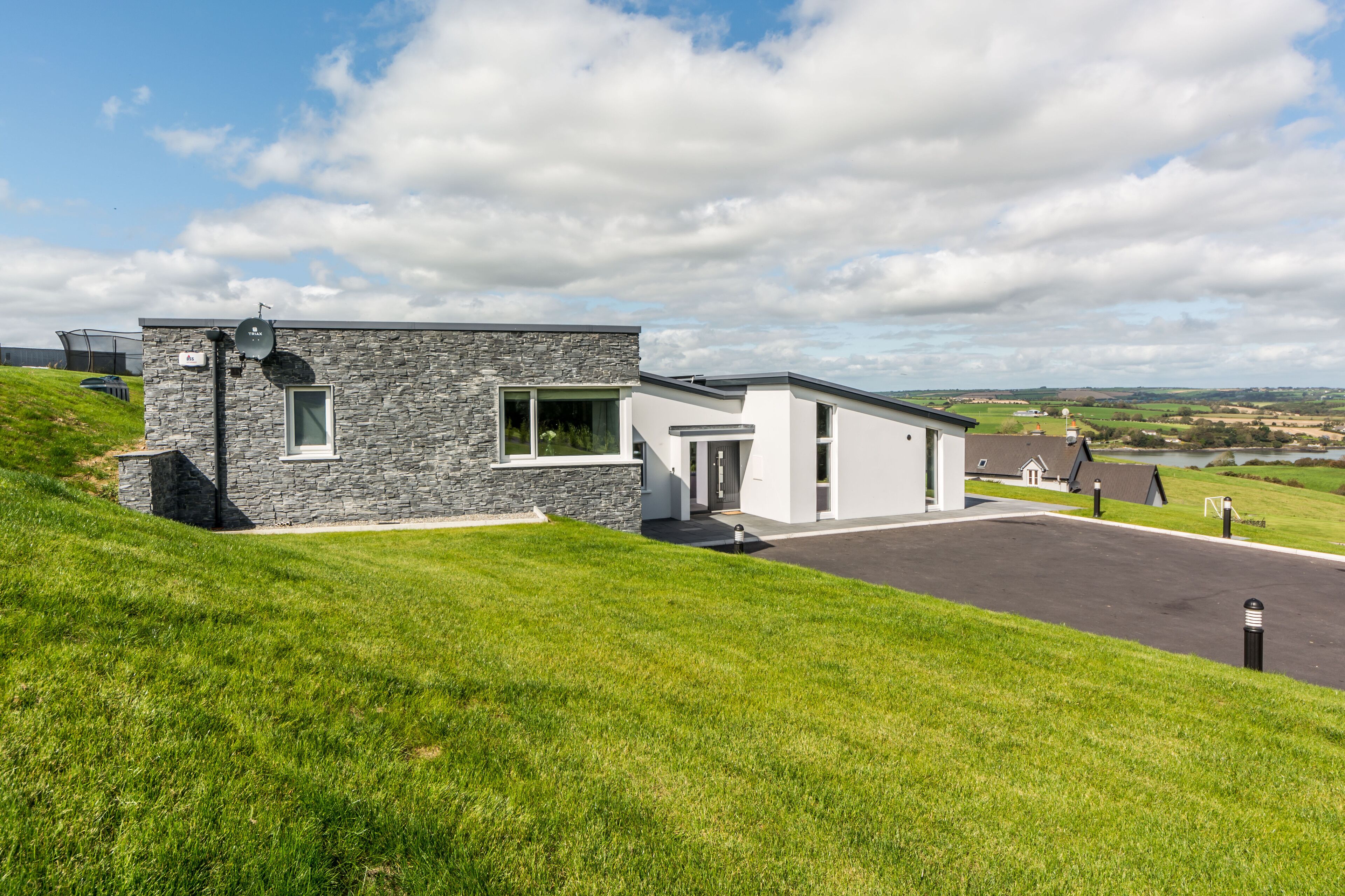 Een modern huis met twee verdiepingen, een gevel van natuursteen, een oprit en uitzicht op het platteland.