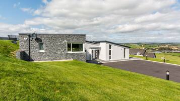 Een modern huis met twee verdiepingen, een gevel van natuursteen, een oprit en uitzicht op het platteland.