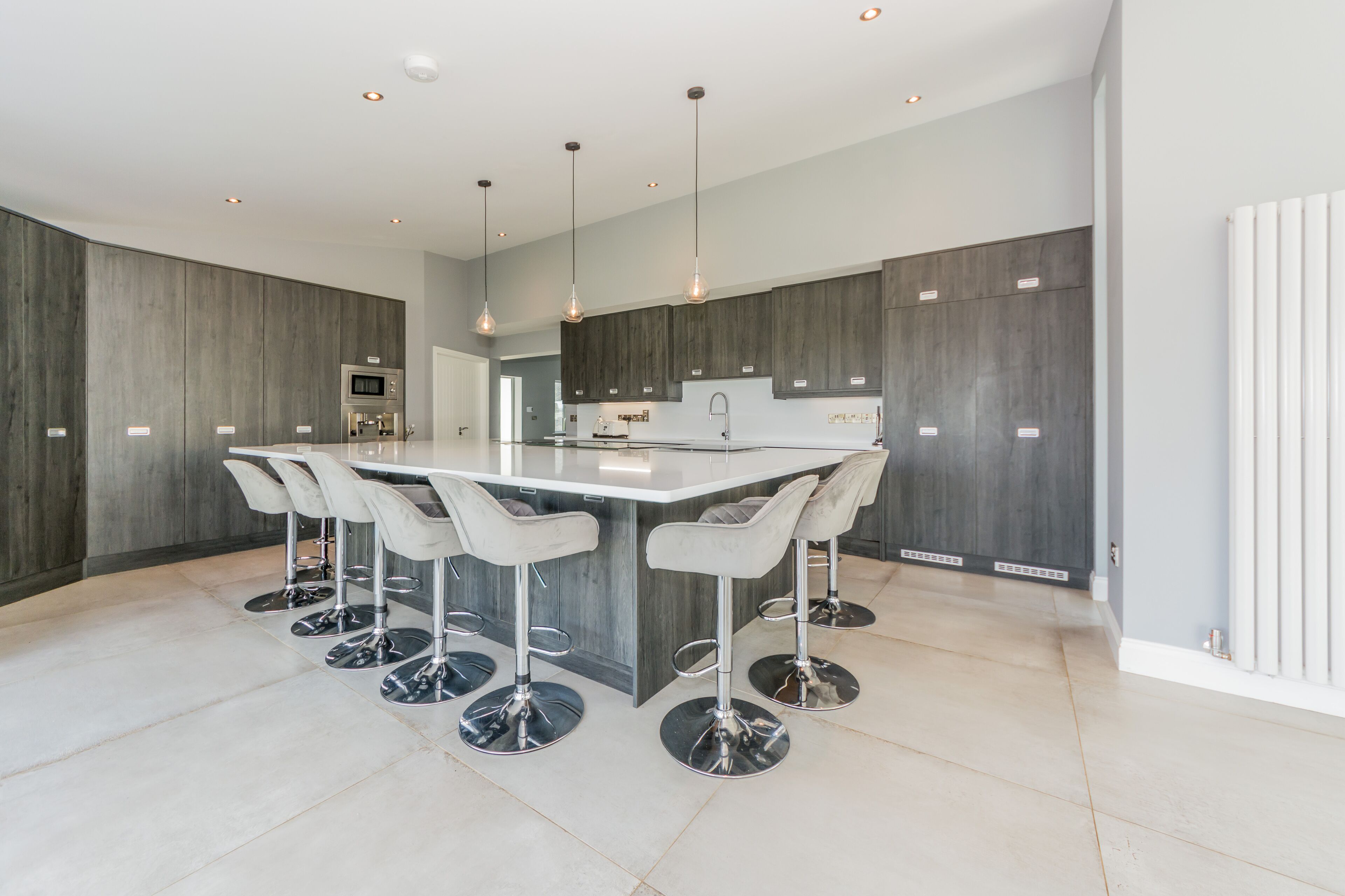 Een moderne keuken met donkerhouten kasten, een centraal eiland met barkrukken en inbouwspots.