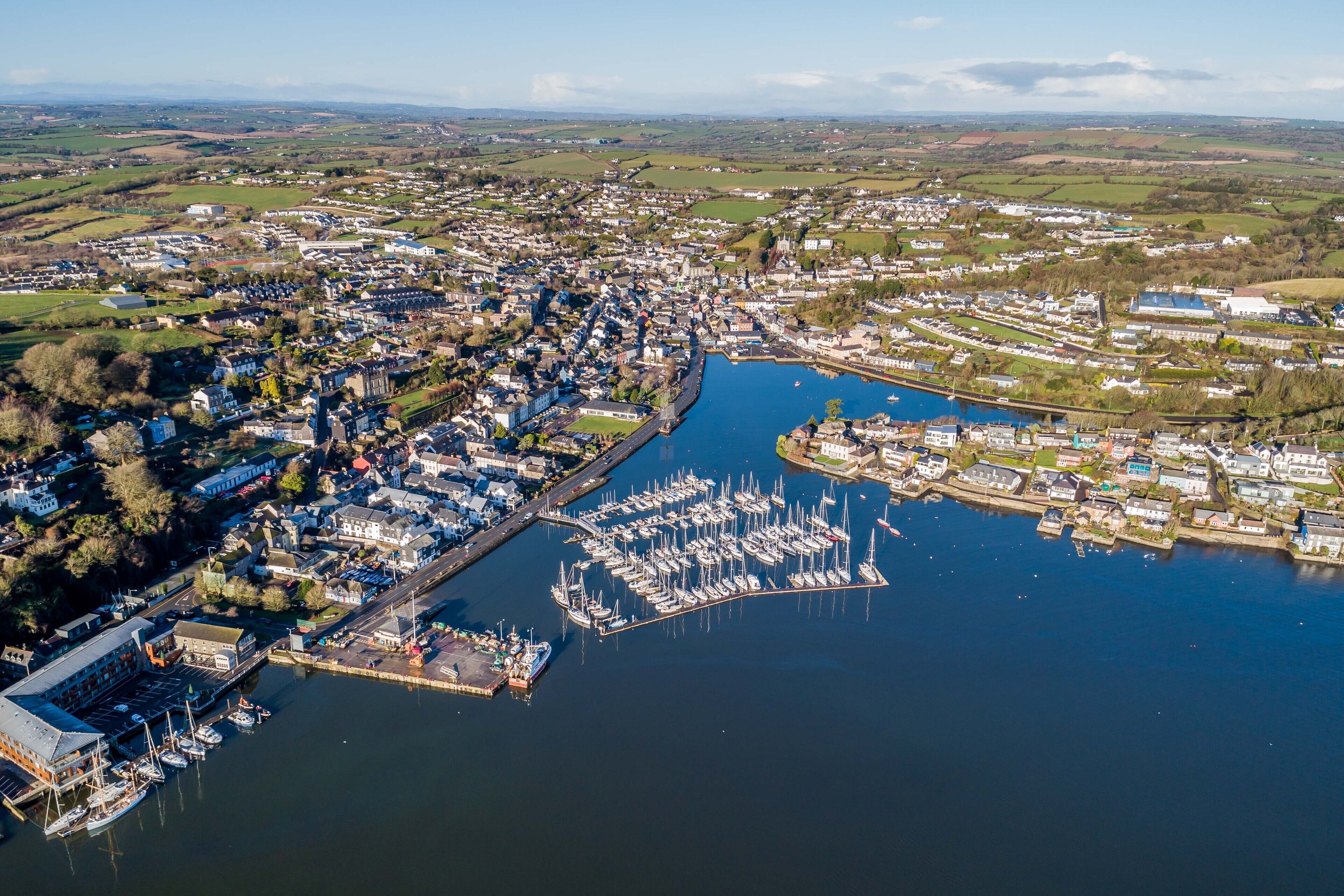 An aerial view of a coastal town with a marina, houses, and surrounding fields.