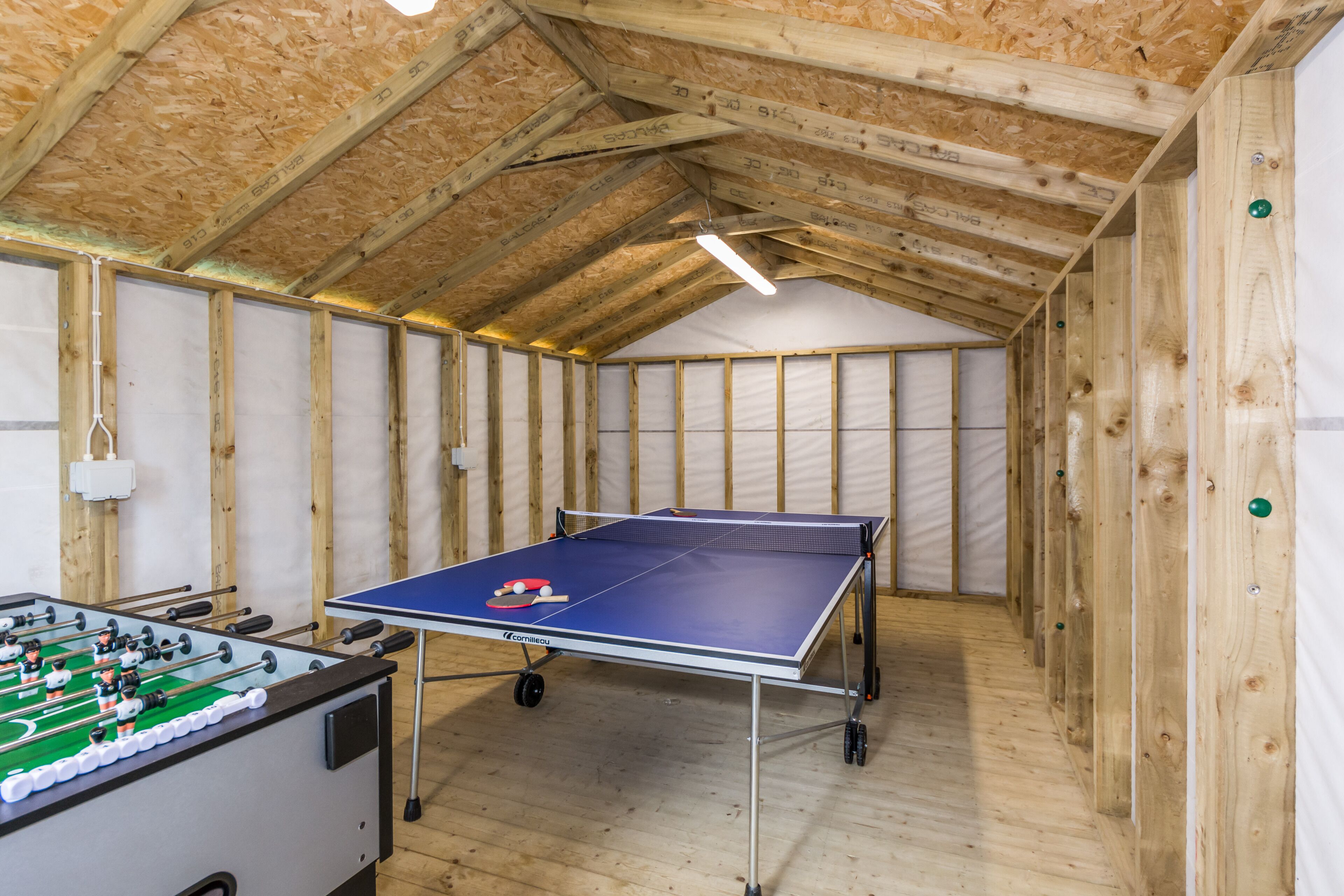 Une pièce avec une table de ping-pong et un baby-foot, des murs en bois et un plafond en pente.