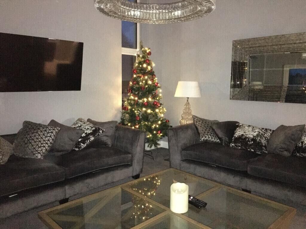 A living room with two grey sofas, a glass coffee table with a remote control, a Christmas tree, and a lamp.