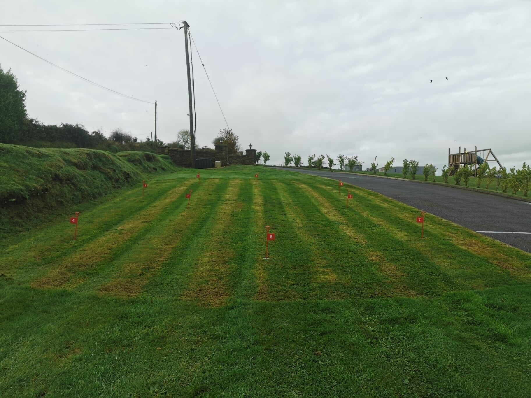 A grassy area with numbered markers, a road, and a playground structure.