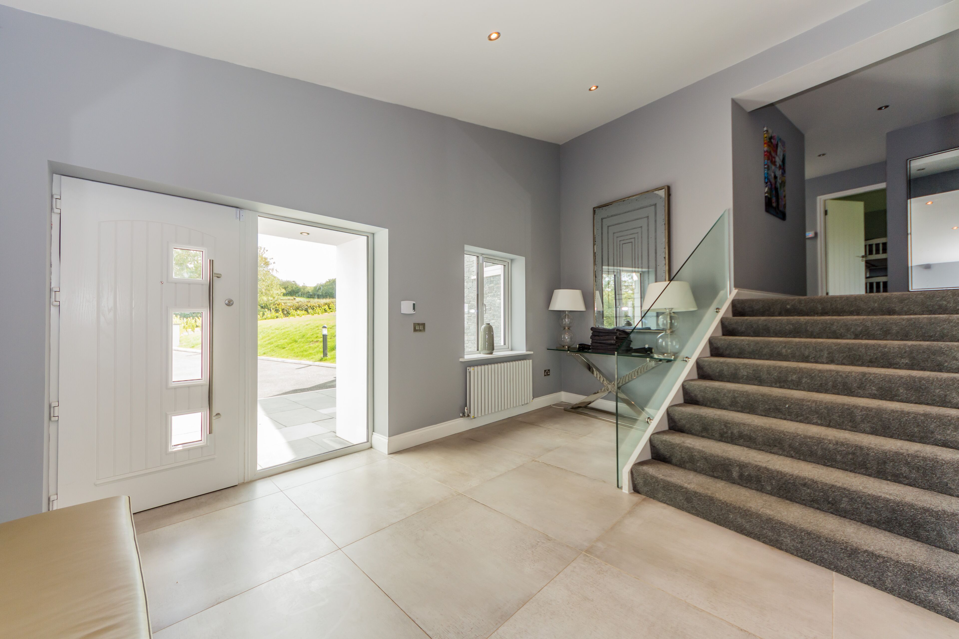 A spacious interior with a staircase leading to a second floor, a glass door leading outside, and a view of greenery.