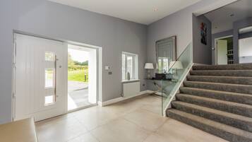 A spacious interior with a staircase leading to a second floor, a glass door leading outside, and a view of greenery.