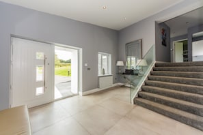 Interior espaçoso com escada que dá para um segundo andar, porta de vidro que leva para o exterior e vista para o verde.