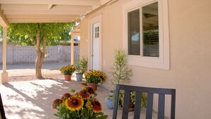 Un espacio de patio cubierto con una mesa, sillas, plantas en macetas y un ventanal.
