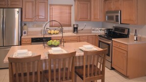 Una cocina con armarios de madera, electrodomésticos de acero inoxidable, una mesa de comedor con sillas y un cartel de bienvenida.