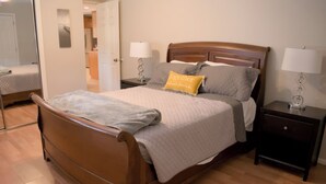 Una cama bien hecha con un cabecero de madera, dos mesitas de noche con lámparas y un espejo en la pared.