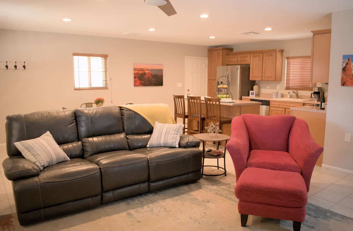 A living room with a black leather sofa, a red armchair, and a dining area with wooden chairs and a table.