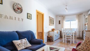 A living room with a blue sofa, a glass coffee table, and a red sofa. There is a kitchen area with a dining table and chairs. - Villa Los Naranjos, oasis with jacuzzi 15 minutes from Seville (Almensilla)