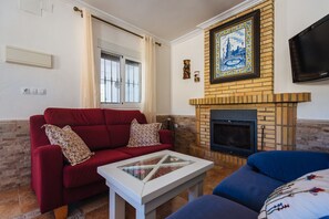 A living room with a red sofa, a blue sofa, a white coffee table, a fireplace, and a TV mounted on the wall.