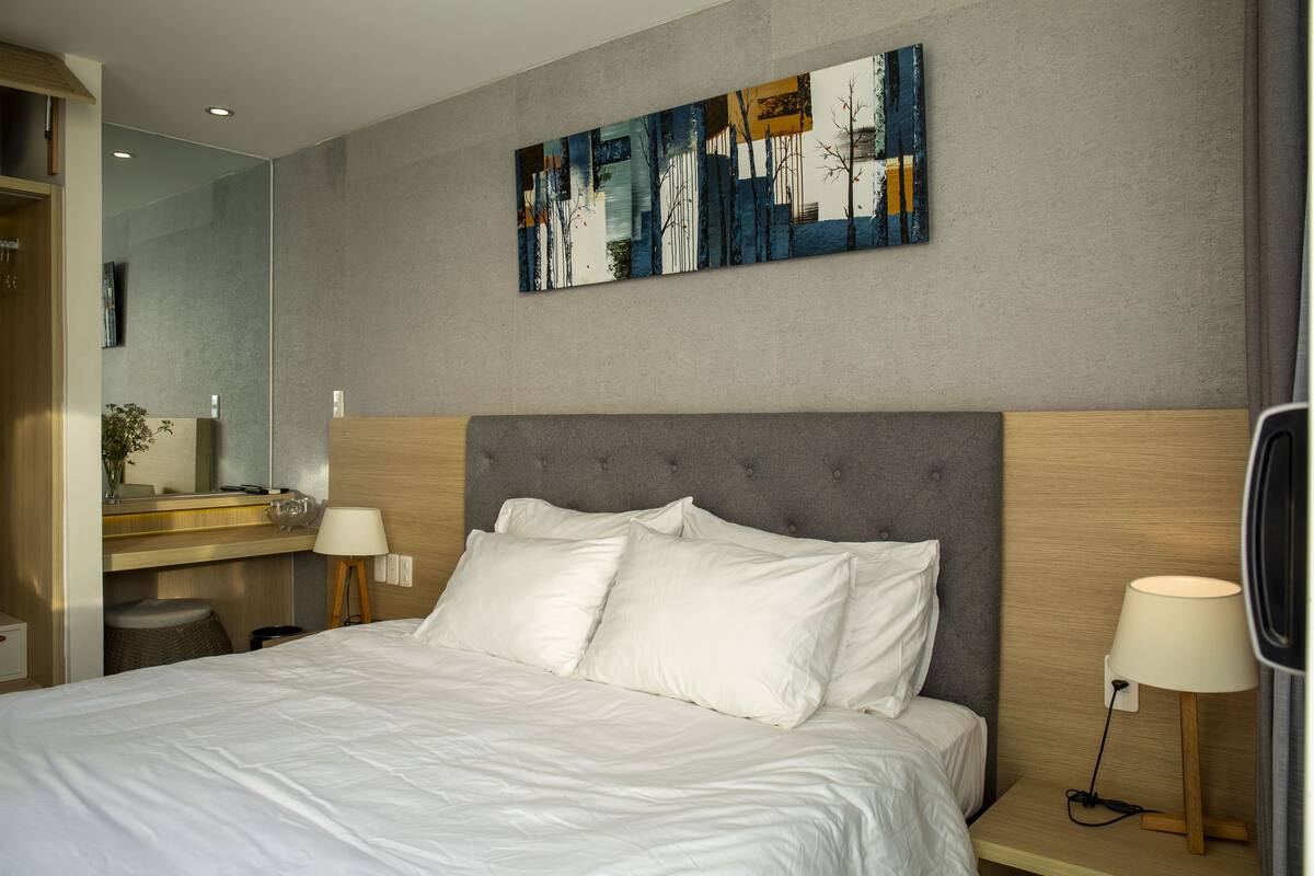 Une chambre d’hôtel moderne avec un grand lit, une table de chevet avec une lampe, un tableau accroché au mur et un miroir.