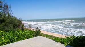 Une vue sur la côte, avec un chemin en béton menant à la plage, le tout entouré de verdure.