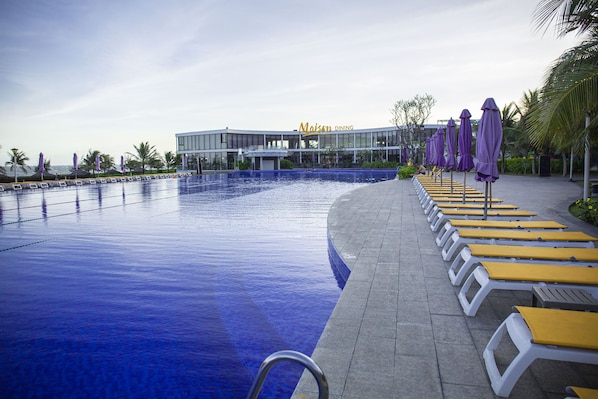 A swimming pool with lounge chairs and umbrellas, a building labeled 'Maison Dining' in the background, and a clear sky.