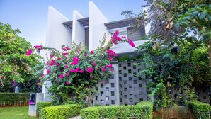 Un bâtiment moderne à la façade géométrique, entouré d’un espace vert bien entretenu et de plantes fleuries.