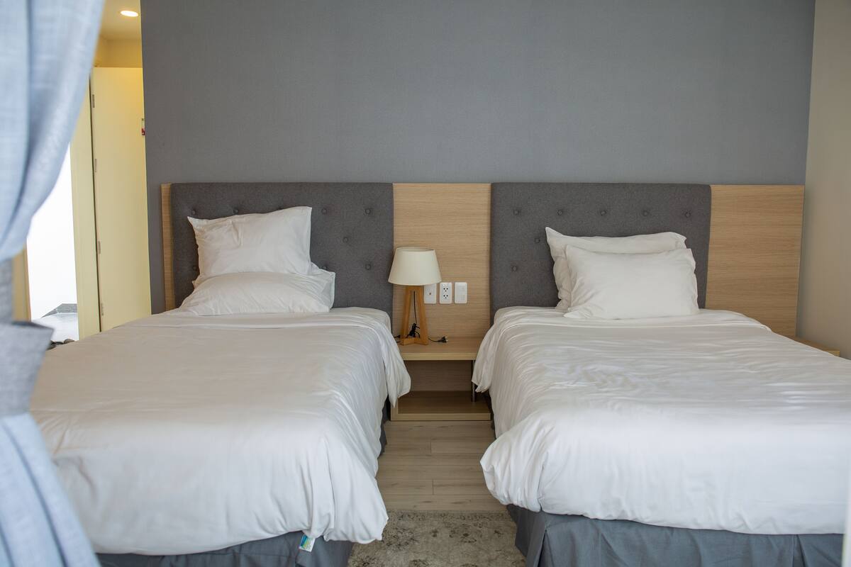 Une chambre d’hôtel avec deux lits, une table de chevet avec une lampe et une tête de lit en bois.