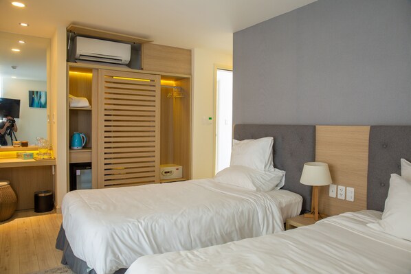 Habitación de hotel con dos camas, un armario de madera, una pequeña kitchenette y un televisor.