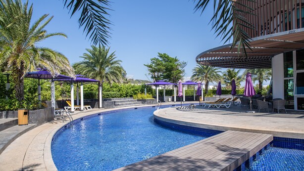 Une piscine entourée de palmiers, avec des chaises longues et des parasols, ainsi qu’un espace de repos abrité.