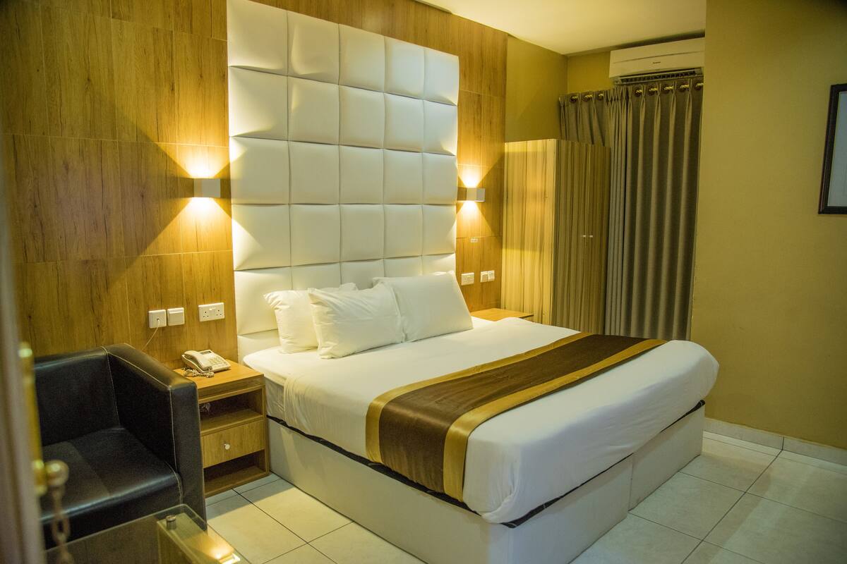 A hotel room with a large bed, wooden paneling, a nightstand with a phone, and a chair.