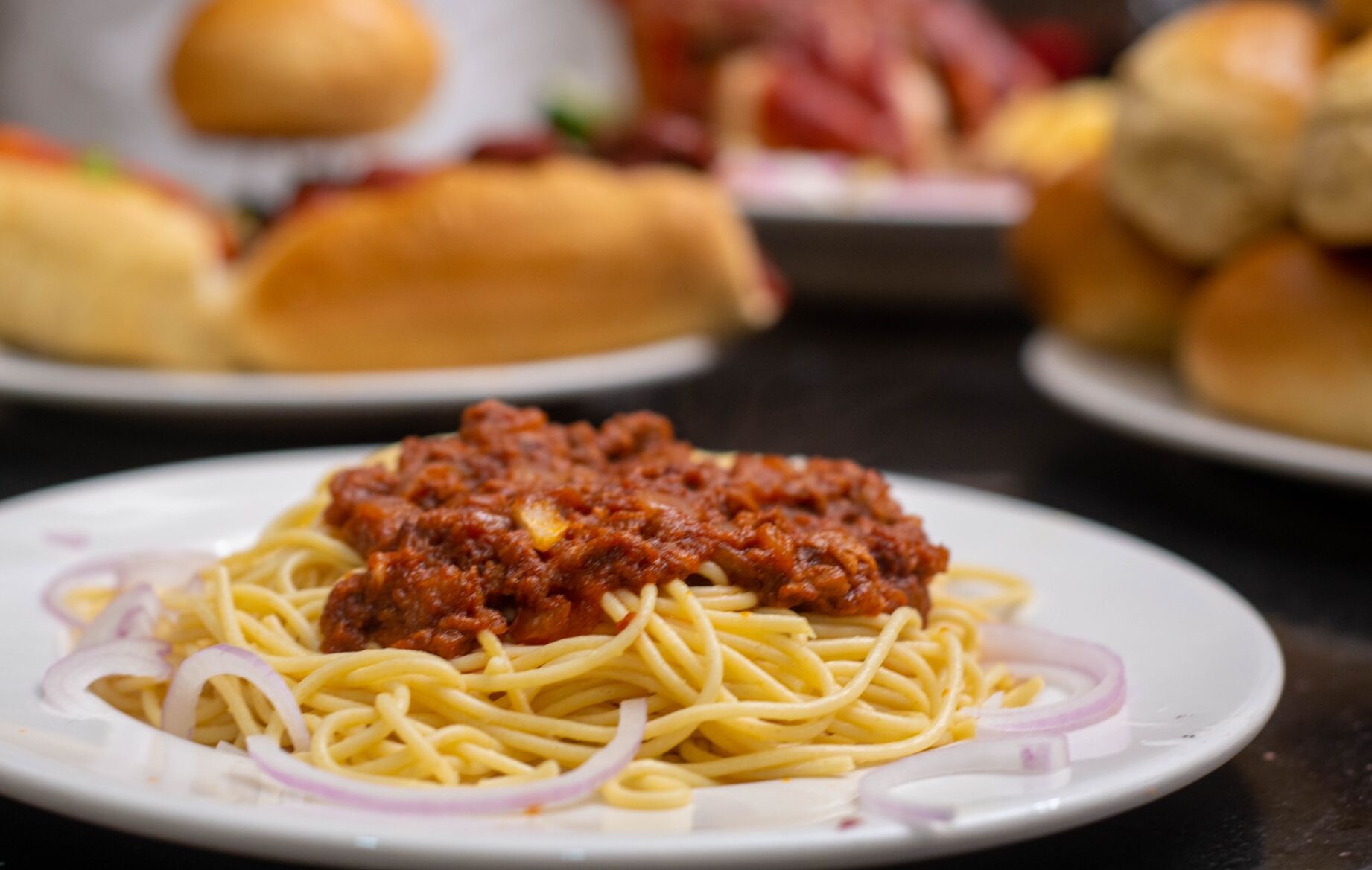 Une assiette de spaghettis avec une sauce à la viande et des oignons en tranches.