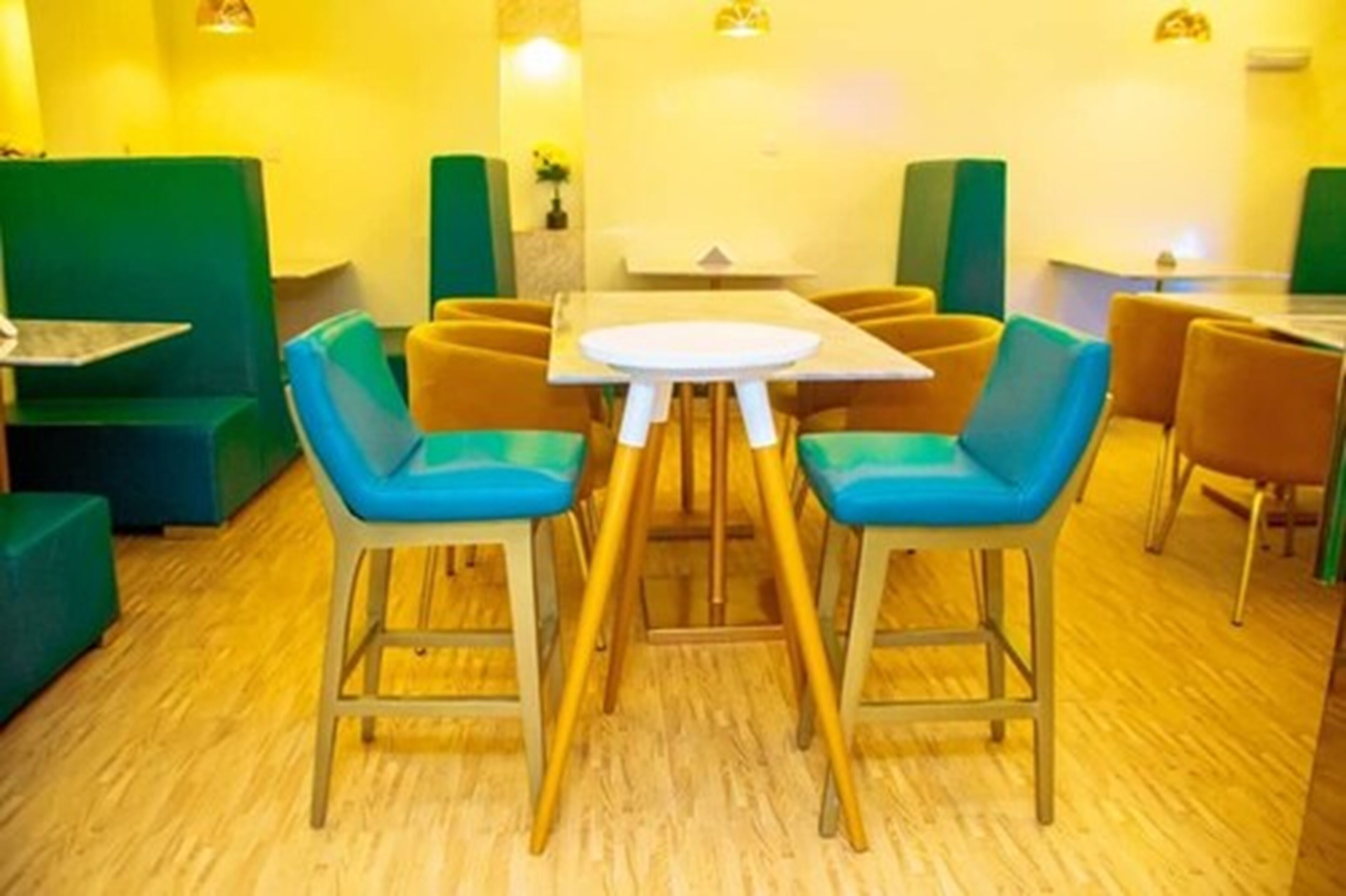 A dining area with green and yellow seating, a round table, and wooden flooring.
