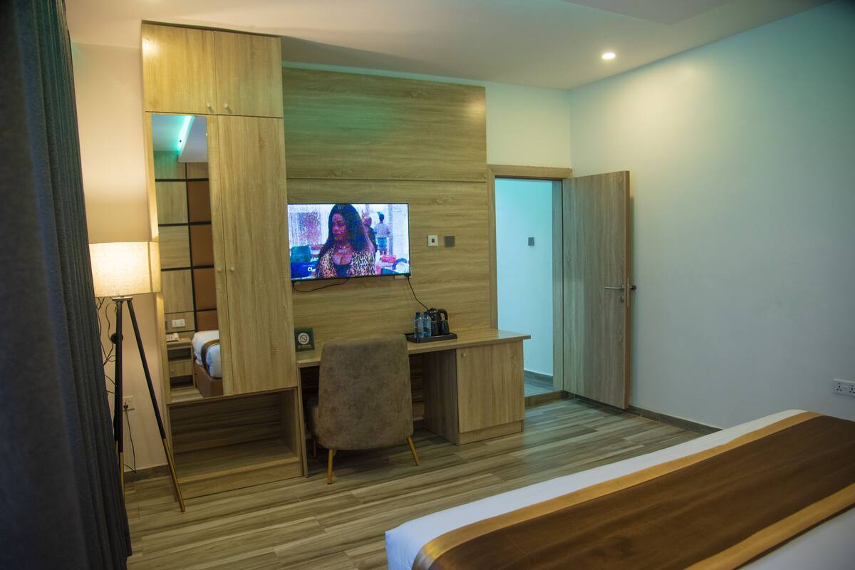 A modern hotel room with a wooden desk, a comfortable chair, a bed, and a television mounted on the wall.