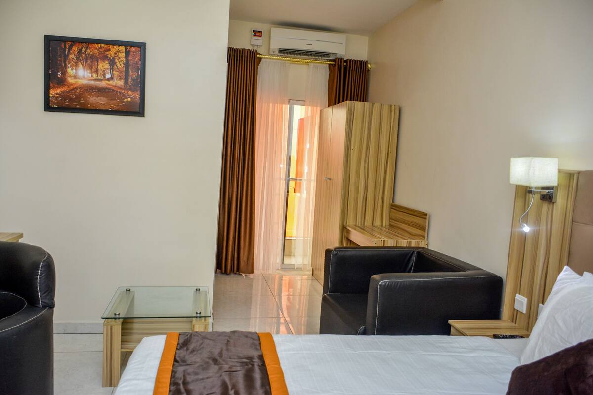 A hotel room with a bed, a desk, a chair, a TV, and a painting on the wall.