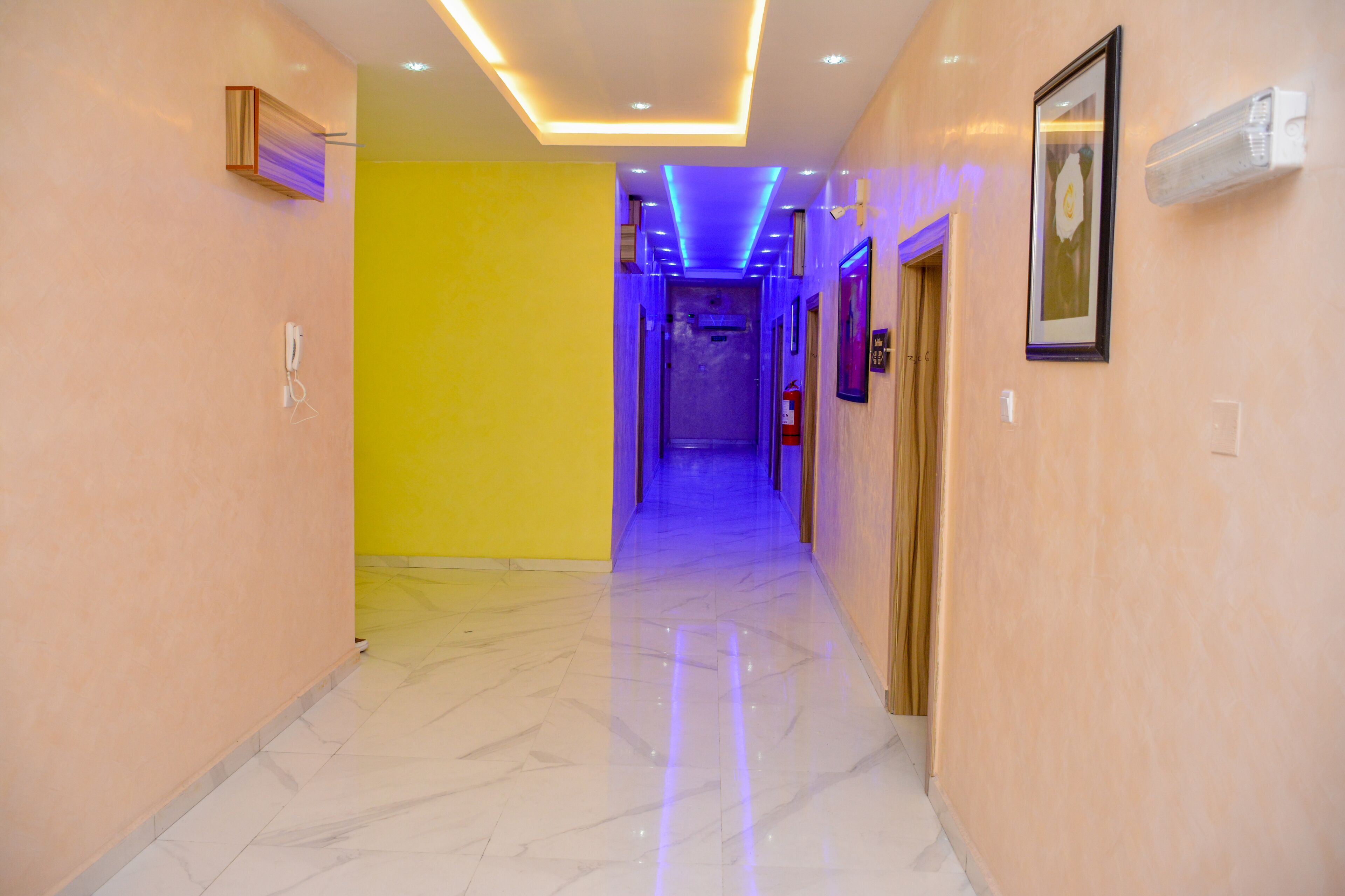 Un pasillo de hotel con piso de mármol, pared amarilla y techo con iluminación azul.