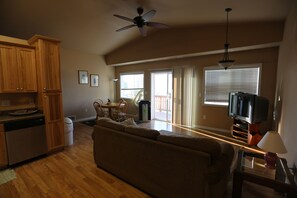 A spacious living area with a wooden floor, a sofa, a dining table with chairs, a ceiling fan, and a television. - Spacious 3-Unit Group Rental - Sleeps Large Groups (Polson)