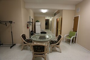 A dining area with a glass-top table surrounded by wicker chairs, a white refrigerator, and a green chair in the corner. - Spacious 3-Unit Group Rental - Sleeps Large Groups (Polson)