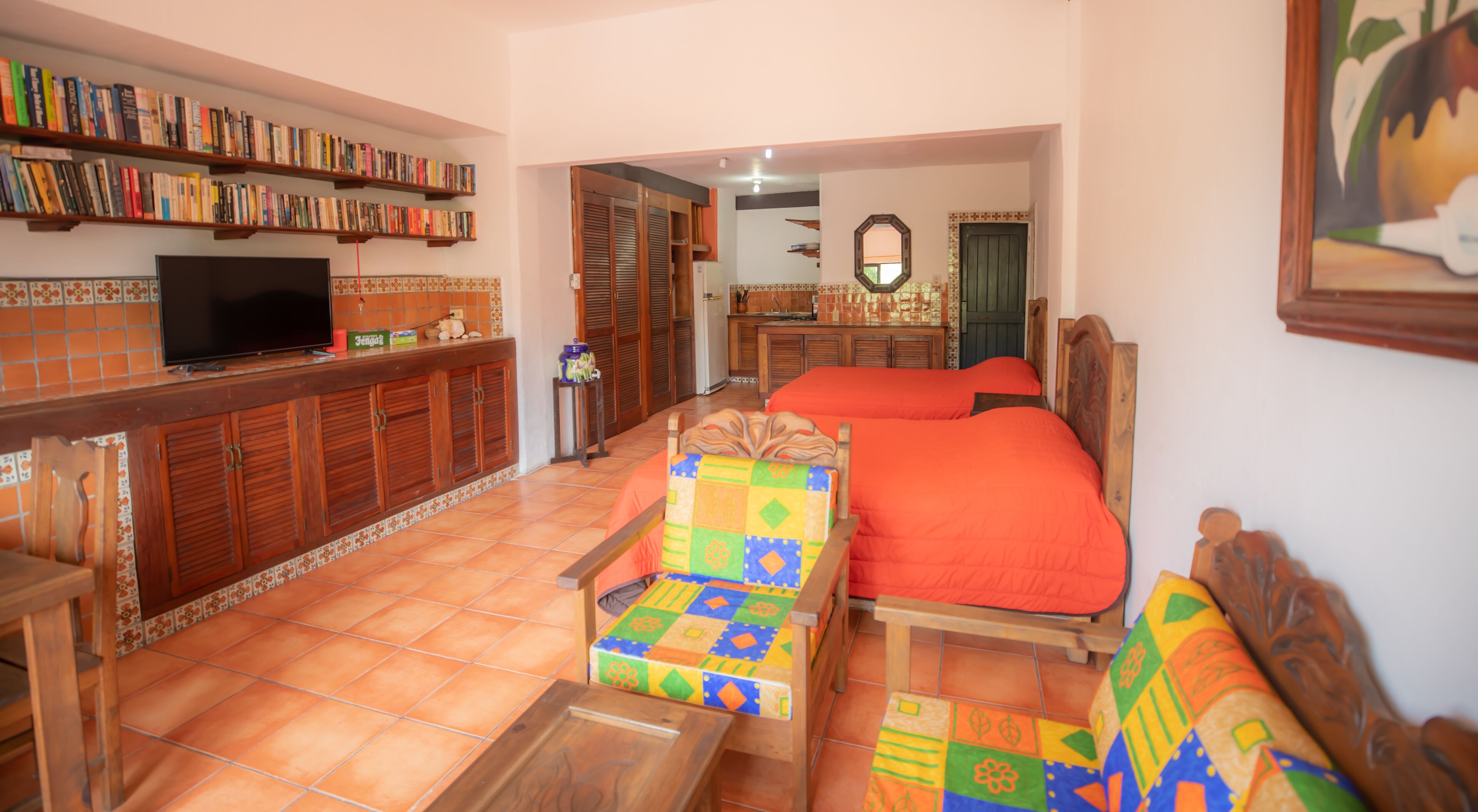 A room with a wooden bed, a colorful chair, a TV on a shelf, and a bookshelf.