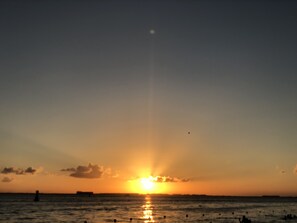 A sunset over a calm sea with a distant shoreline and a few people swimming. - Beach FrontFully  Equipped Suite # 4 (Centro - Supmza. 001)