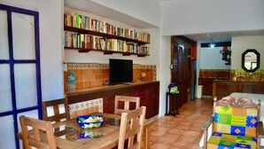 A dining area with a wooden table, chairs, and a colorful cushion. A bookshelf with books is visible in the background. - Beach FrontFully  Equipped Suite # 4 (Centro - Supmza. 001)