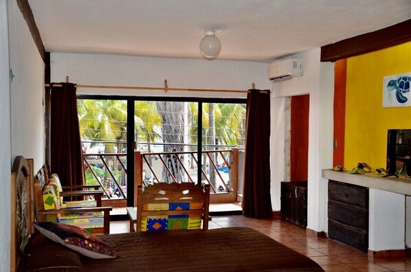 A room with a wooden bed, a small table, and a view of palm trees through large windows.