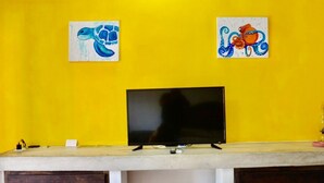 A room with a yellow wall, a flat-screen TV on a wooden stand, and two paintings of sea creatures.