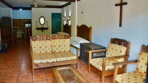 A room with a sofa, a bed, a wooden chair, a small table, and a cross on the wall.