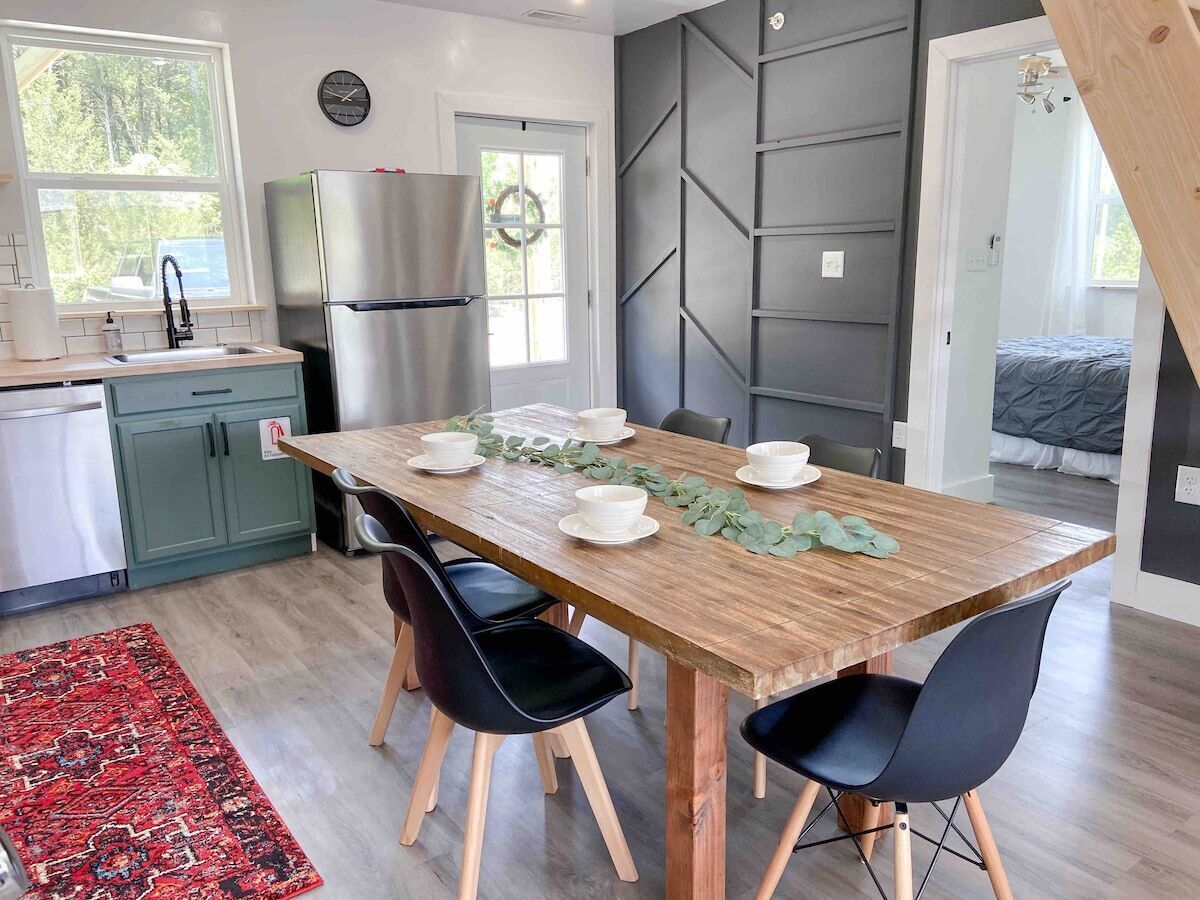 Une cuisine moderne avec une table à manger en bois, des chaises noires et un réfrigérateur en acier inoxydable.