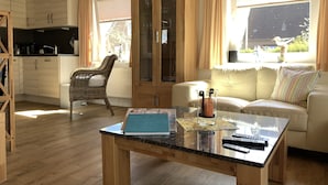 A cozy living area with a sofa, a wicker chair, a glass coffee table, and a kitchen in the background. - Maxe house, Paula house - golf course, beach and surfing area within walking distance (Wulfen)