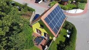 A yellow house with a solar panel roof, a paved driveway, and a small patio with outdoor furniture. - Maxe house, Paula house - golf course, beach and surfing area within walking distance (Wulfen)