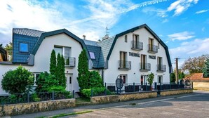 A modern two-story building with a white facade, named "Thermal Panjo." It features balconies, a stone facade, and is surrounded by greenery. - Thermal Panzió Sárvár (Sarvar)