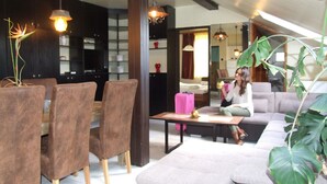 A modern living room with a sofa, chairs, a dining table, and a kitchen area in the background. - Thermal Panzió Sárvár (Sarvar)