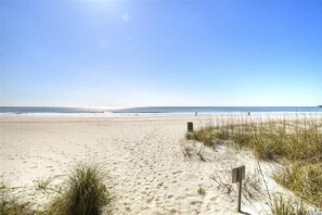 Une plage de sable avec un ciel dégagé, un panneau indicateur et une végétation clairsemée.