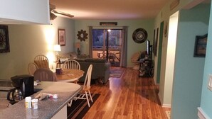 A living room with a fireplace, a dining area with a table and chairs, and a kitchen area with a counter and appliances. - Perfect Vacation Getaway! Beach Condo in Quiet Setting, CLOSE TO THE BEACH! (Myrtle Beach)