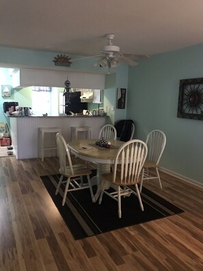 Un coin repas avec une table ronde, des chaises blanches et un ventilateur de plafond.